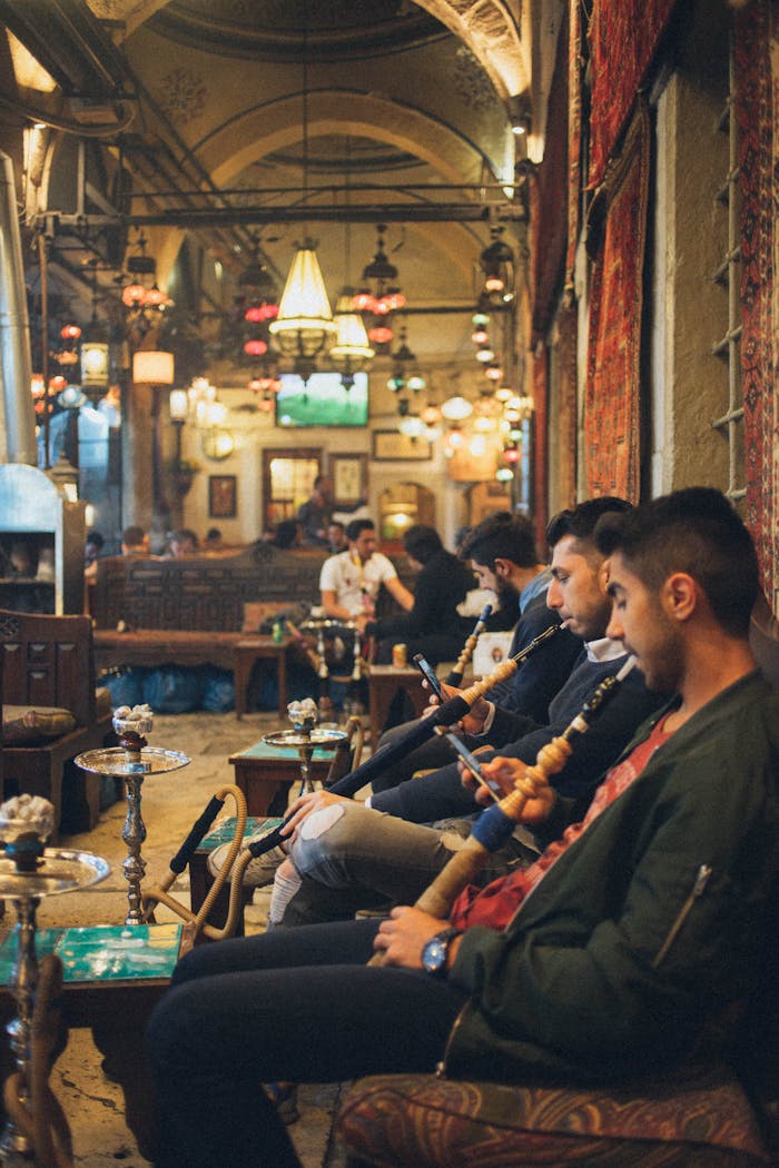 About Group of young men relaxing with hookahs in a cozy, vibrant indoor lounge setting.